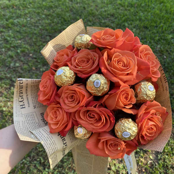 Orange rose bouquet with gold-wrapped chocolates in newspaper-style paper