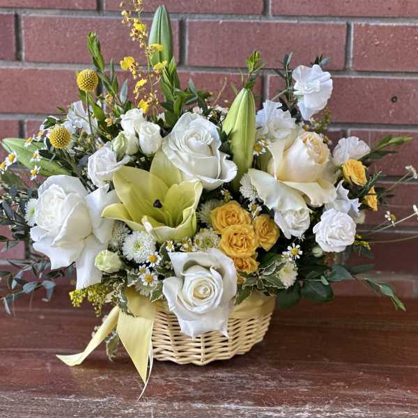 Basket arrangement of white and yellow flowers with a ribbon