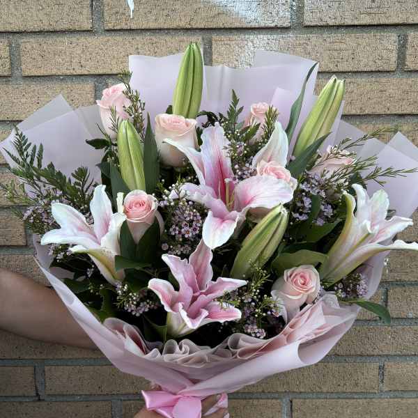 Pink roses and lilies in a wrapped bouquet with a satin ribbon
