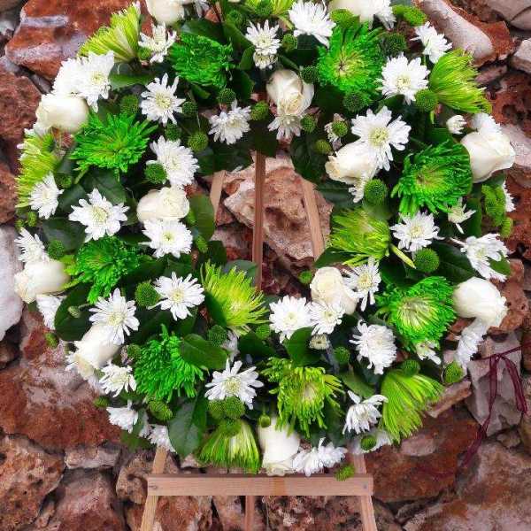Circular floral wreath with white and green flowers on a wooden stand