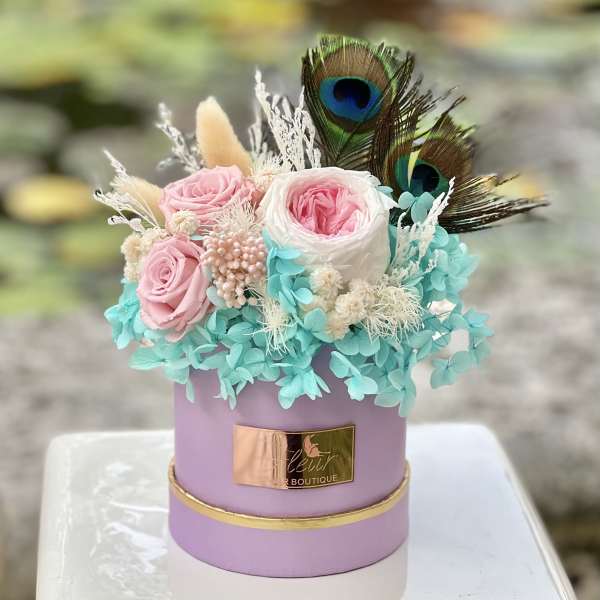 Pink and white roses in a lavender hatbox with peacock feathers