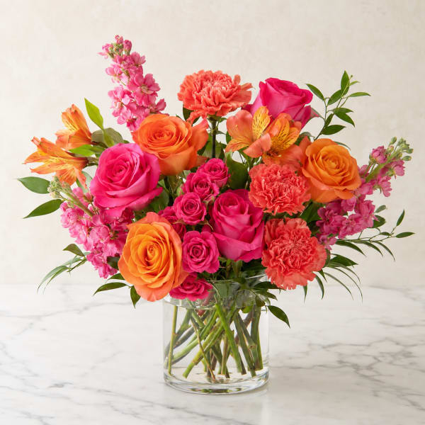 Bouquet of pink and orange roses, carnations, and alstroemeria in a clear glass vase