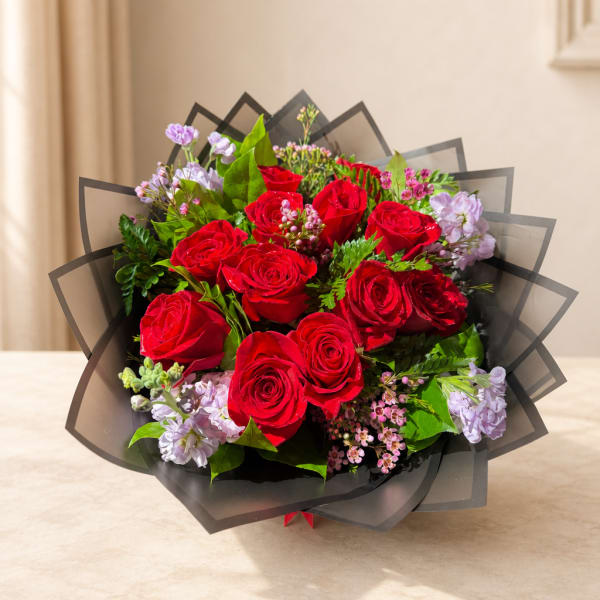 Bouquet of red roses with light purple flowers wrapped in black paper