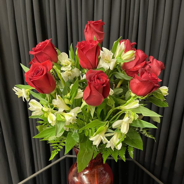 Red roses and white alstroemeria arranged in a red glass vase.