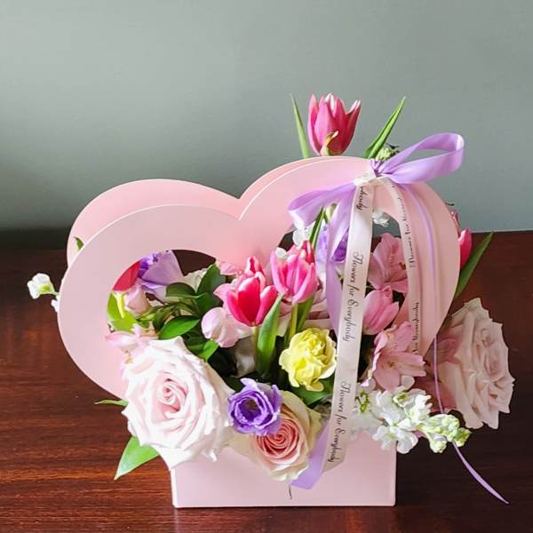 Pink and purple flower arrangement in a heart-shaped box with ribbon