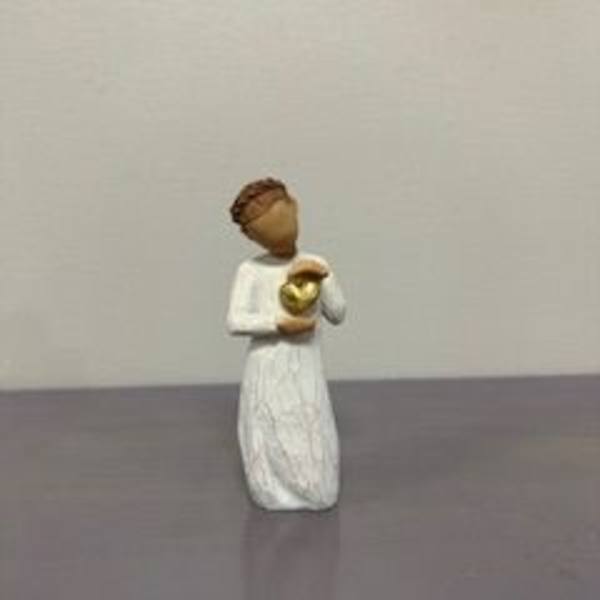 Small angel figurine in a white dress holding a gold heart
