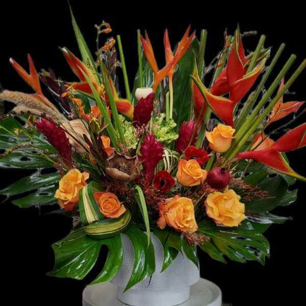 Tropical floral arrangement with orange roses and red heliconia in a white vase