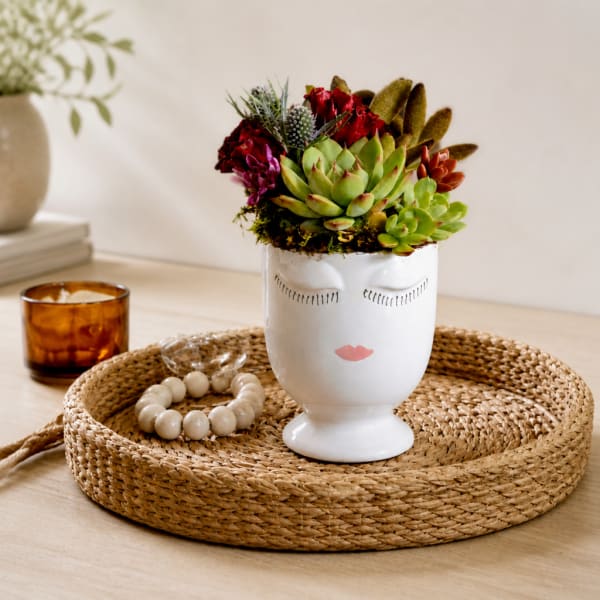 Succulent arrangement in a white face-shaped vase on a woven tray
