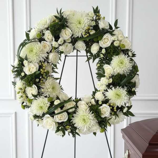 White floral funeral wreath on a black stand beside a casket