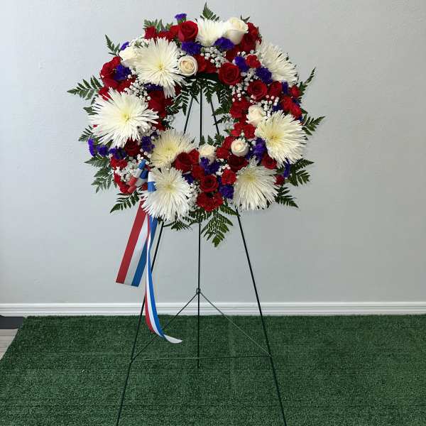 Circular red, white, and blue floral wreath on a stand