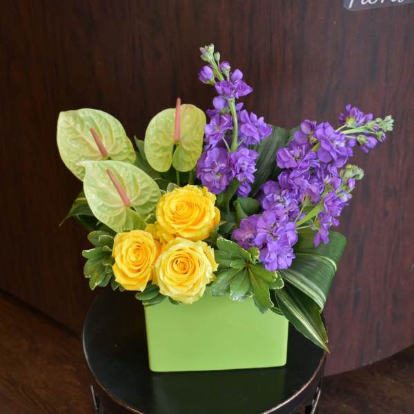 Yellow roses and purple flowers in a green square vase
