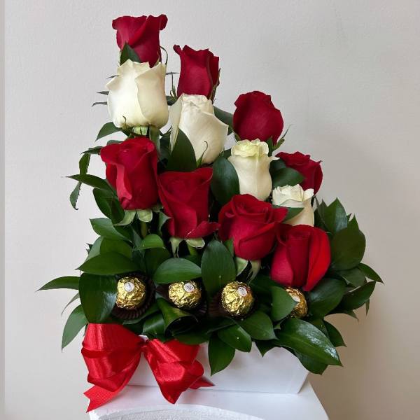 Red and white roses arranged with chocolates and a red ribbon