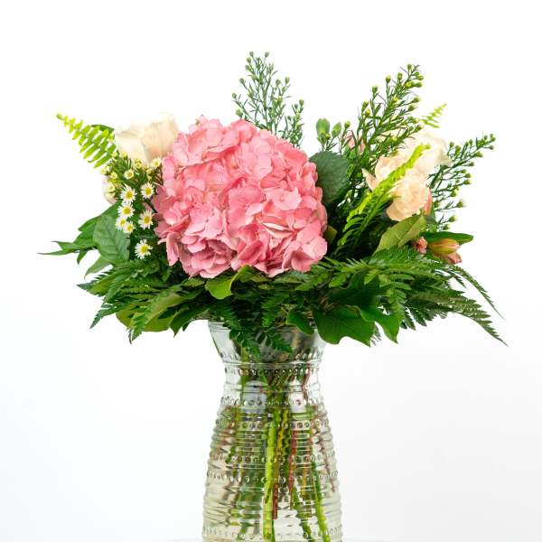 Pink hydrangea bouquet with cream roses in a clear glass vase