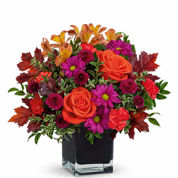 Bright mixed bouquet in a square glass vase with orange roses and purple daisies