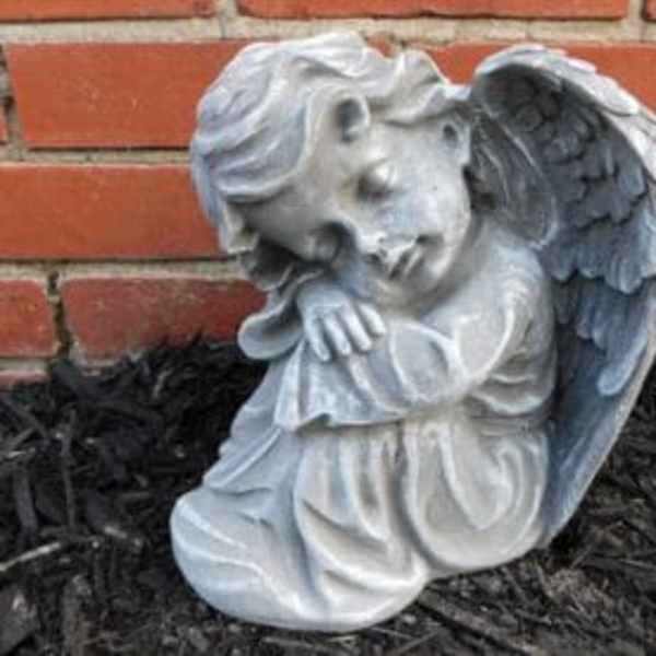 Small stone angel statue with folded wings resting its head on its arms