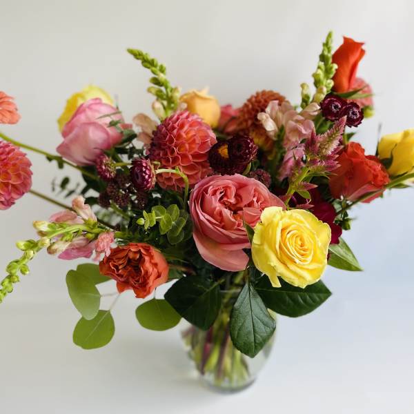 Mixed bouquet of roses, dahlias, and zinnias in a clear glass vase