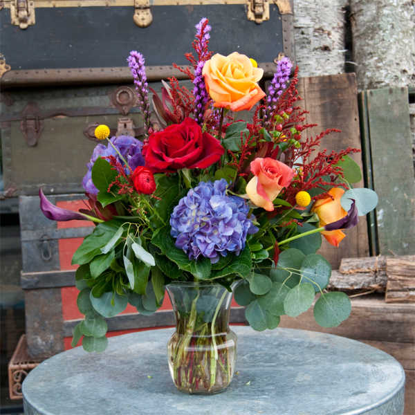 Mixed bouquet of roses, hydrangea, and calla lilies in a glass vase