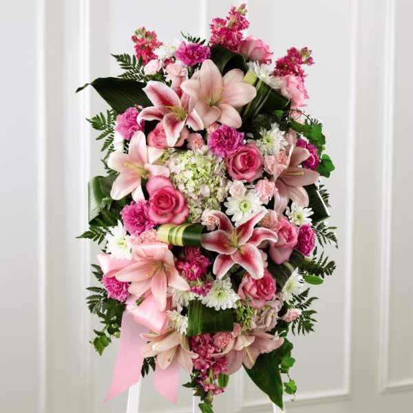 Standing spray of pink lilies, roses, carnations, and white daisies on an easel.