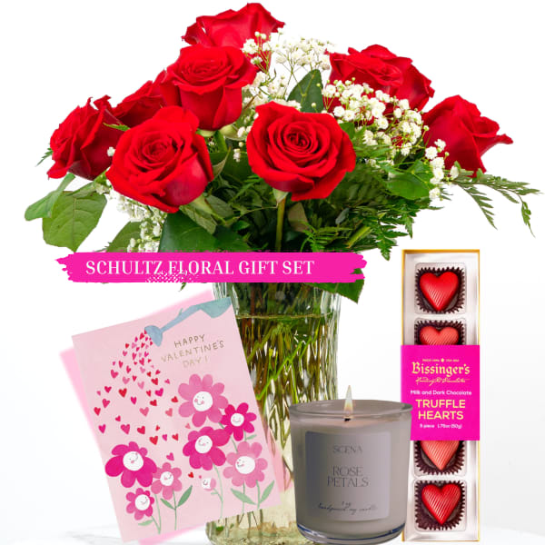 Red roses in a glass vase with a Valentine card, candle, and chocolate hearts