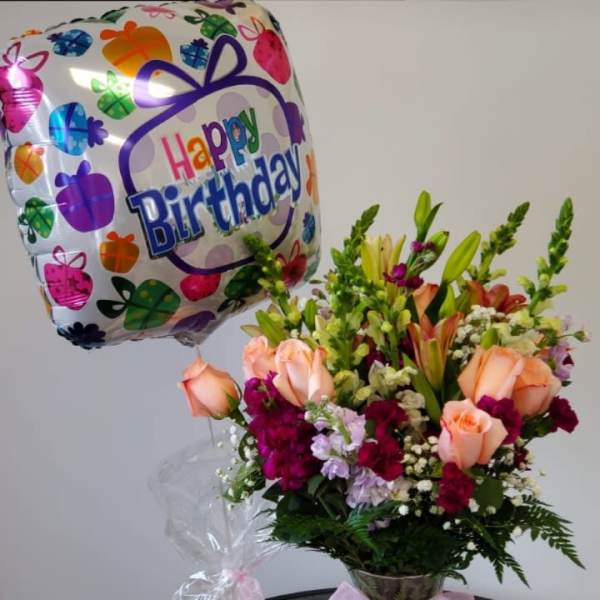 Birthday balloon beside a mixed flower bouquet in a glass vase and a small gift bag