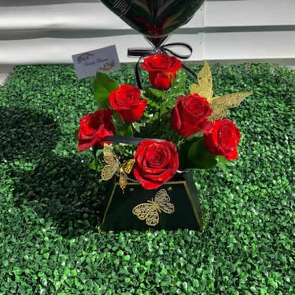 Black heart balloon above red roses in a black vase