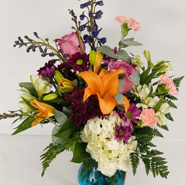 Mixed bouquet in a blue glass vase with orange lilies and pink flowers
