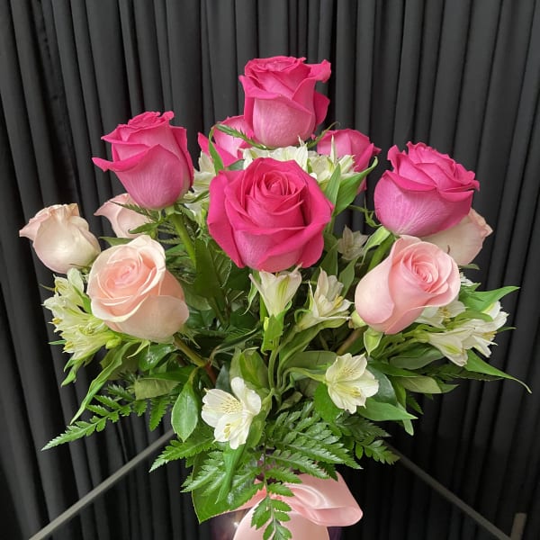 Pink and blush roses arranged in a glass vase with a pink ribbon.