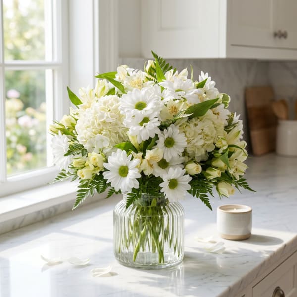 White daisies and pale blooms arranged in a clear glass vase