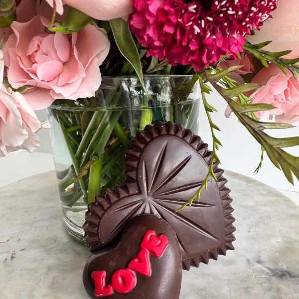 Pink flowers in a glass vase with heart-shaped chocolates in front