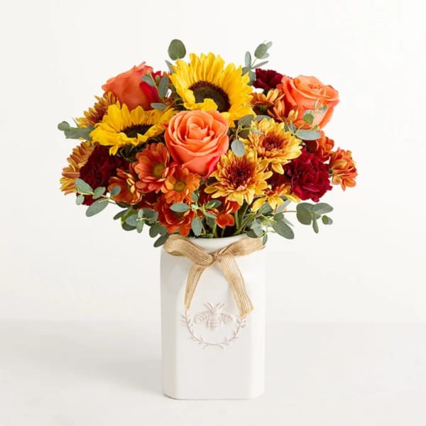 Orange roses and yellow sunflowers in a white vase with a ribbon
