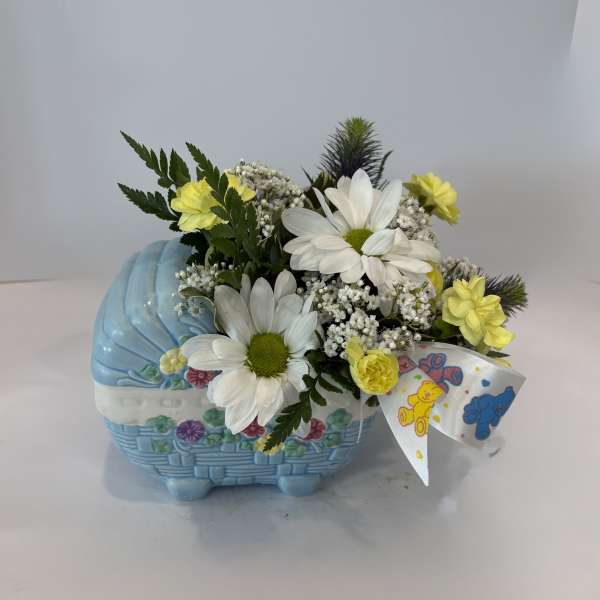 Yellow and white flowers arranged in a blue basket with a teddy bear ribbon