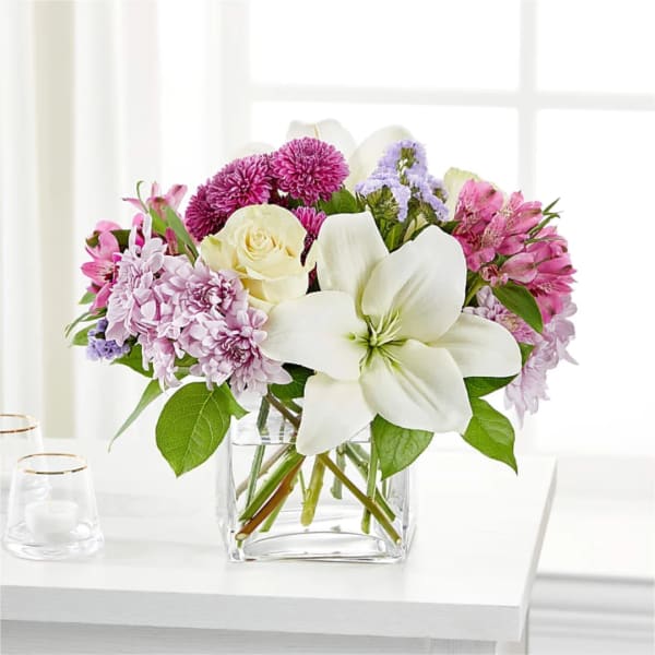 Mixed bouquet of white lilies, cream roses, and pink-purple flowers in a clear glass vase
