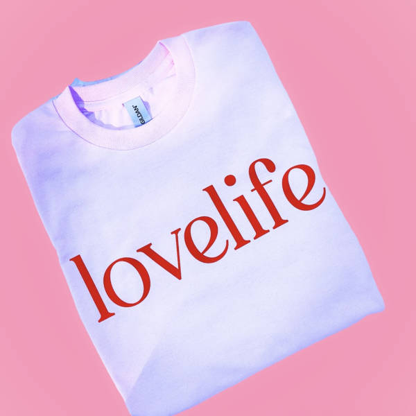 Folded white sweatshirt with red "lovelife" text on a pink background