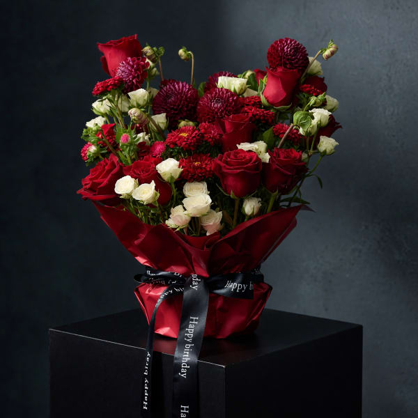 Red roses and white spray flowers in red wrap with a birthday ribbon