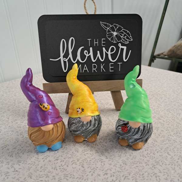 Three colorful gnome figurines displayed in front of a flower market sign