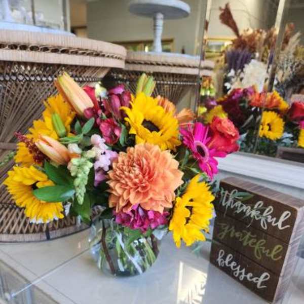 Bright mixed bouquet with sunflowers, lilies, and gerbera daisies in a glass vase