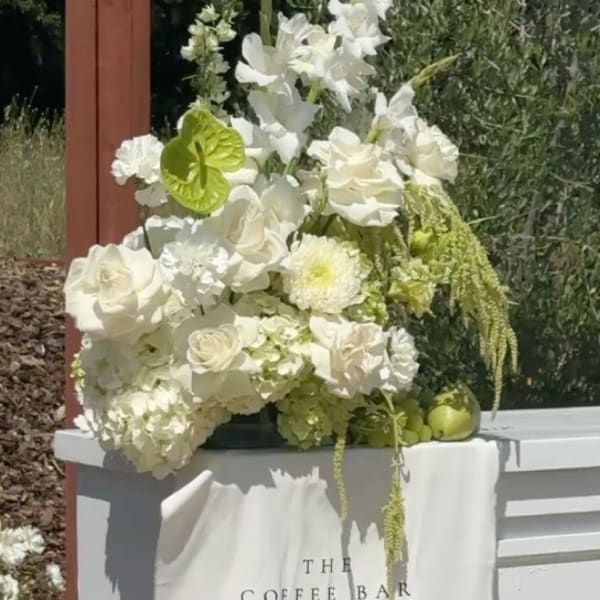 White floral arrangement with roses and orchids on a coffee bar table