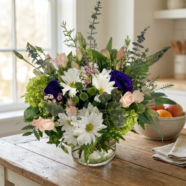 Mixed bouquet of white daisies, pale pink roses, and green blooms in a glass vase