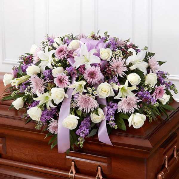Lavender and white casket spray of roses, lilies, and mums with ribbon on a wooden casket