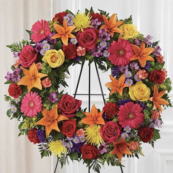 Colorful floral wreath on a black easel with roses, lilies, and daisies