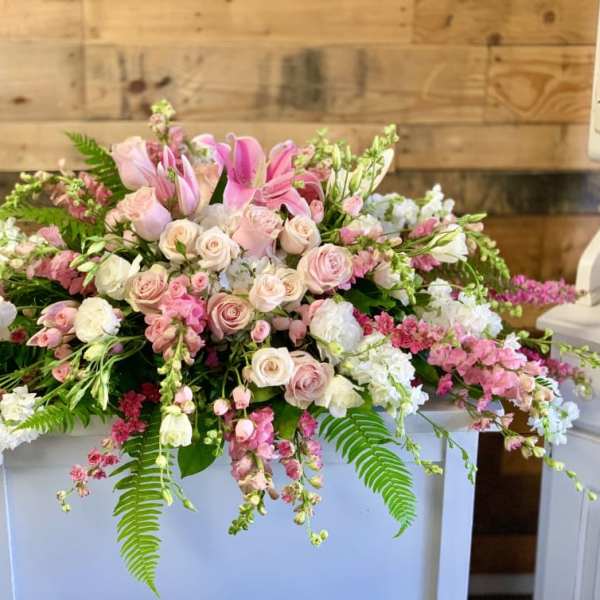 Large pink and white floral arrangement with roses and lilies on a white pedestal