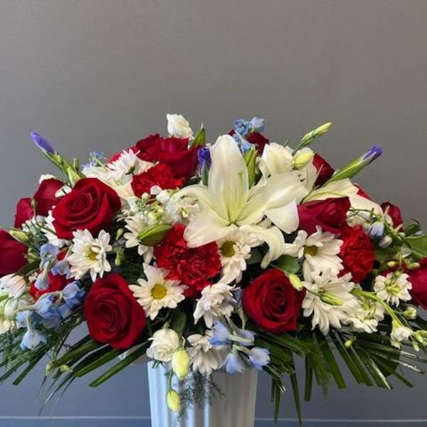 Red roses and white lilies in a white vase with small white and blue flowers