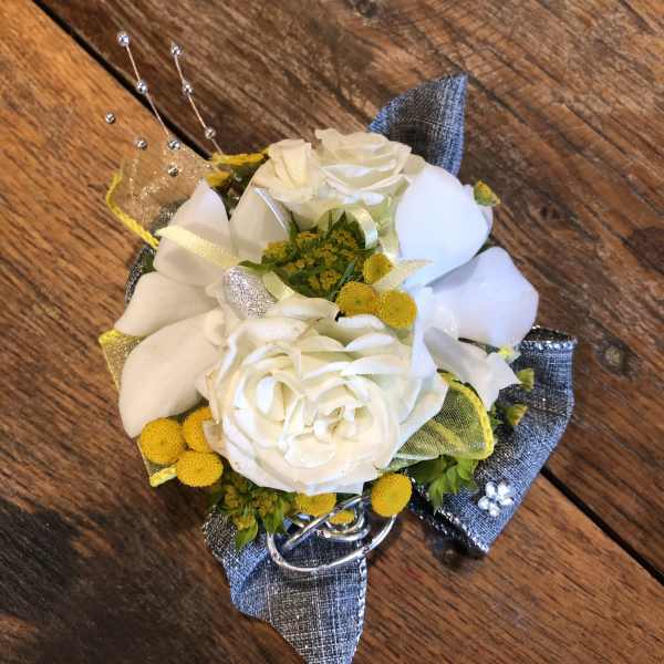 White rose corsage with yellow accents and silver ribbon on a wooden surface