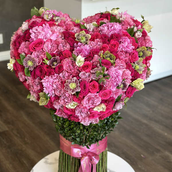 Large heart-shaped bouquet of pink and magenta roses with a ribbon-wrapped stem bundle