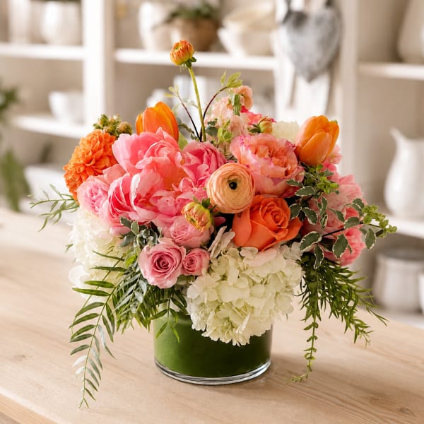 Mixed pink and orange flower arrangement in a green glass vase