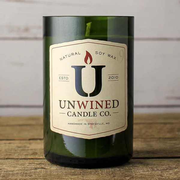 Green glass jar candle with cream label reading Unwined Candle Co. on a wooden surface