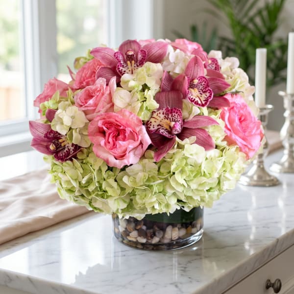 Pink roses and orchids arranged in a glass vase with pale hydrangeas