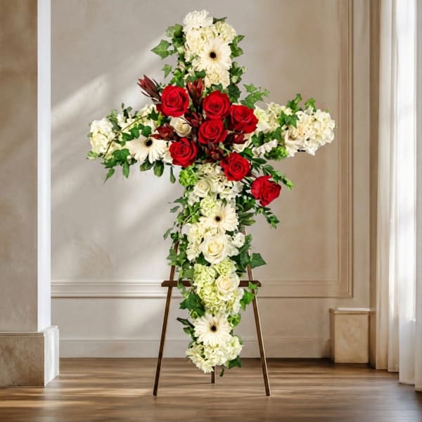 Cross-shaped floral arrangement with red roses and white flowers on an easel