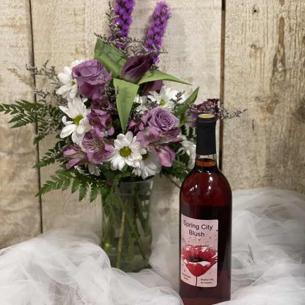 Purple and white bouquet in a glass vase beside a bottle of wine