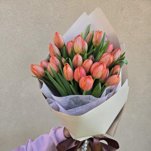 Bouquet of pink-orange tulips wrapped in cream paper with a ribbon